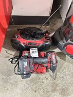 Drill with battery, charger, and boombox grouped on garage floor