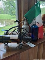 All items on windowsill: two syphon bottles, cast iron holder with wine bottle, Italian flag