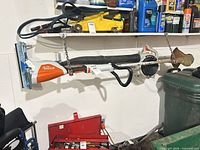 Stihl FSA 57 cordless trimmer with brush head hanging on wall