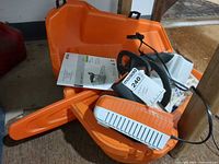 Chainsaw, charger, manual, bar scabbard inside open orange hard case