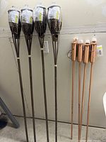 Front view of four bamboo and four copper tiki torches leaning against wall