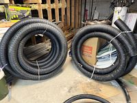 Two coiled black corrugated drain pipes