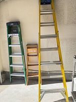 Three ladders side by side: green Louisville step ladder, yellow fiberglass extension ladder, wooden step stool