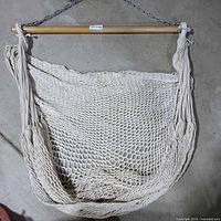 Full view of cotton rope hammock chair spread across floor showing seat, ropes, wooden spreader bar, and chain