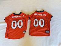Back view of two orange Broncos pet jerseys showing team name and number 00