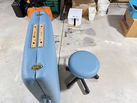 Closed massage table showing light blue vinyl exterior with brass latches and adjustable stool