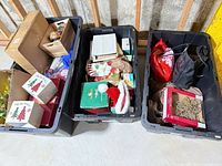 Three large black totes filled with boxed ornaments, stockings, garland and bags