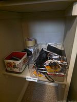 Shelf with floral tin, two tape rolls, clear tray holding batteries, umbrella, flashlight