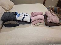 Four stacks of assorted sweaters, cardigans and blazers laid out on bed