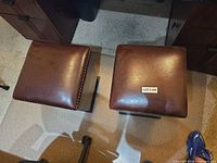 Top view of both brown faux leather stools showing nailhead trim and surface wear