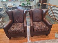 Front view of both leather and fabric wingback chairs showing cushions, arms, nailhead trim, wood legs