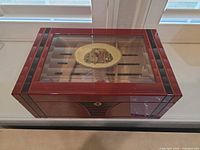 Closed humidor exterior showing red mahogany lacquer, black inlays and glass top with logo