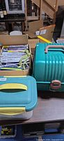 Stacked containers including Sassaby case, teal-lid box and cardboard box of packaged zippers