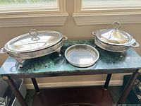 Two oval covered chafing dishes and one round dish on tabletop