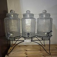 Front view showing three glass dispensers with lids and shared metal stand