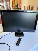 Front view of Vizio 26-inch TV on stand with remote and power cord visible
