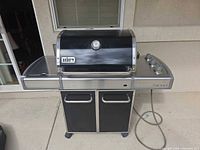 Front view of Weber Genesis grill closed, showing lid, thermometer, side shelf, control panel, cabinet, hose