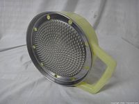 Angled view showing stainless steel grating surface and plastic handle