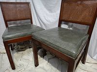 Front view of two mid-century wooden chairs with cane backs and grey vinyl seats
