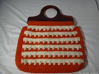 Front view of crocheted purse showing orange body, white stripe pattern, amber handles