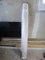 Full view of sealed roll of white poly sheeting leaning against wall