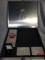 Open metal case showing embossed lid, foam interior and contents