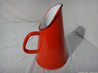 Right side view of red enamel pitcher showing handle and conical shape