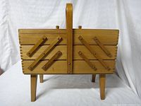 Front view of wooden cantilever sewing box showing legs, handle, and diagonal brace strips