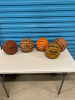 All five basketballs on table against blue backdrop