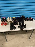 Entire lot of children’s shoes displayed on table, multiple brands and styles visible
