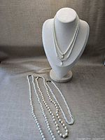 Bust displaying two necklaces and three additional necklaces laid flat