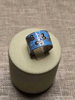 Ring front view on display stand showing enamel butterfly pattern