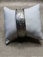 Front view of sterling silver floral engraved bangle on display pillow