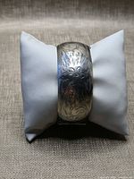 Front view of engraved sterling silver bangle on display pillow
