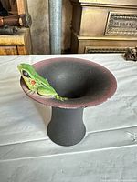 Angled view of black pedestal bowl showing green frog on rim