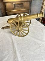 Left side view of brass cannon showing wheels and barrel