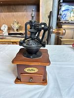 Front view of cast iron manual coffee grinder showing crank wheel, wooden base and drawer