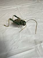 Side view of green enamel metal grasshopper figurine