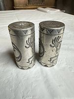 Front view of both pewter shakers showing Kokopelli motif and patina