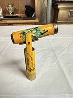 Front view showing graphic of uniformed youth on yellow tin barrel and pivoting handle