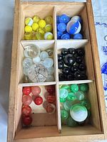 Top view of wooden box showing yellow, blue, clear, black, red and green marbles in six compartments