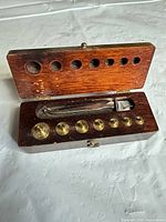 Open wooden case showing brass weights, 50 g block and tweezers