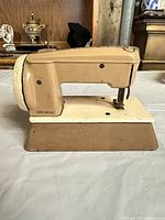 Left side view of beige miniature Singer sewing machine on integral base