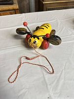 Top view of yellow wooden bee pull toy showing face, wings, wheels, and pull string