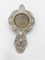 Front view showing ornate handle, floral scroll designs, mesh bowl