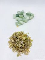 Pile of light yellow cube and chip beads in foreground, pale green polished beads in background