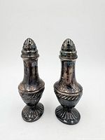 Front view of both silver plated shakers showing engraved designs and tarnish