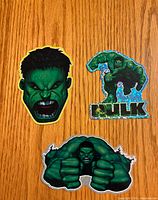 Front view of all three Hulk stickers on wood surface