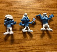 Front view of three Smurf figurines showing sunglasses, mirror, and arm positions