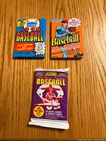 Front view of three sealed baseball card packs: 1990 Fleer, Donruss puzzle & cards, 1991 Score Series 2.